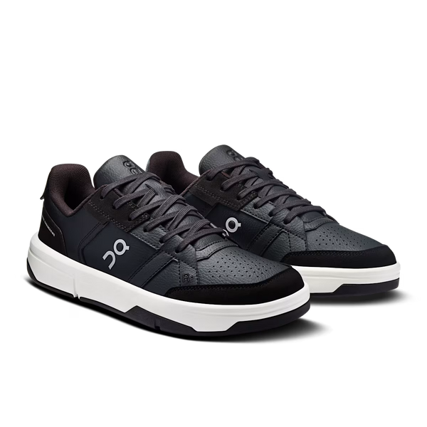 A pair of On sneakers in black and dark gray with a white midsole, shown from a three-quarters angle on a white background.
