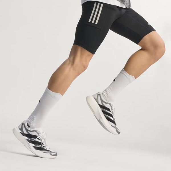 Person wearing black athletic shorts with white stripes, white socks, and black and white sneakers on a light gray background.