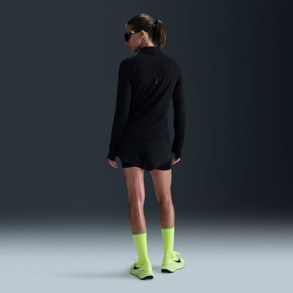 Person wearing a black athletic outfit with neon green socks and shoes on a dark background