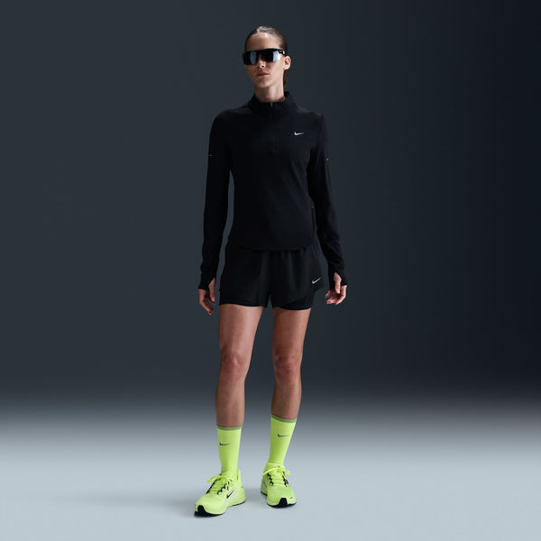 Person wearing a black athletic outfit with neon green socks and shoes on a dark background
