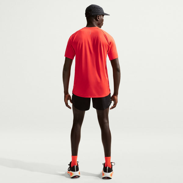 Person wearing a bright orange athletic shirt and black shorts on a light gray background
