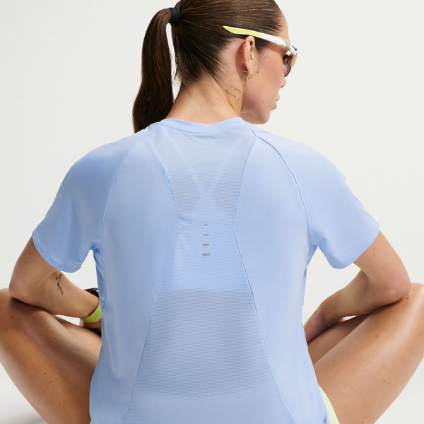 Woman wearing a light blue athletic shirt sitting on the ground with a neutral background