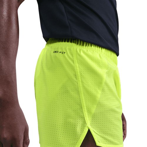 Close up of a person wearing bright yellow athletic shorts with a brand logo on a white background