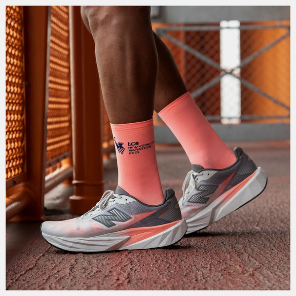 Person wearing gray running shoes with orange accents and matching socks on a textured surface.