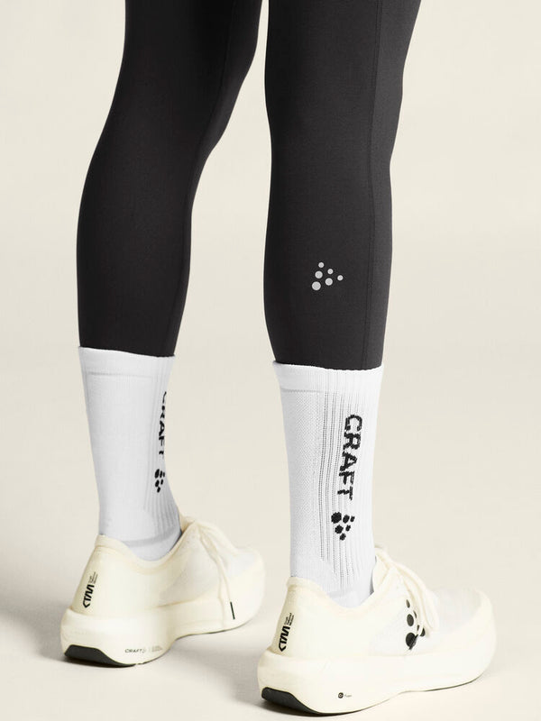 Person wearing black leggings with a visible brand logo, white socks, and white shoes on a neutral background.