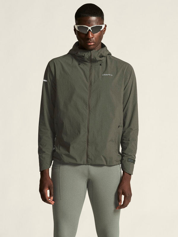 Person wearing a green jacket and pants with sunglasses on a beige background