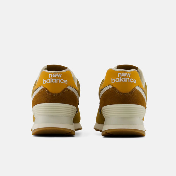 A pair of New Balance sneakers shown from the back, featuring a mustard yellow and brown suede upper with cream midsoles and white 'new balance' branding on the heel.