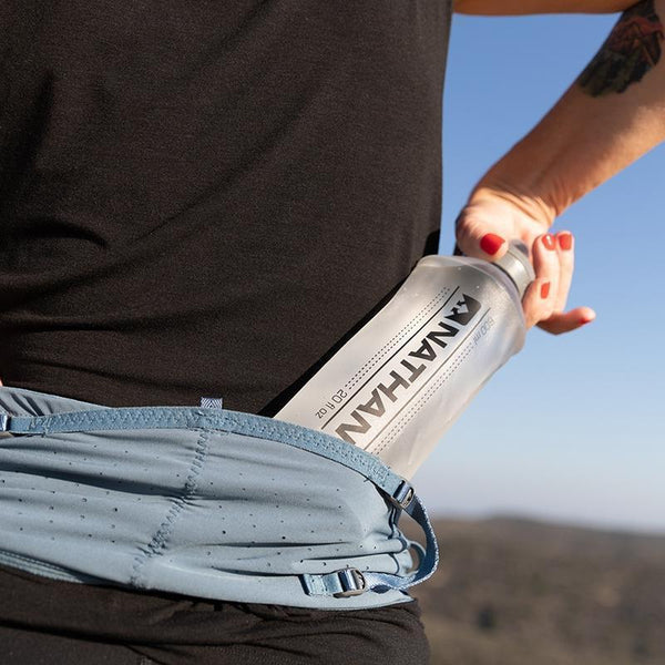 Zoomed in view of a water bottle going in one of pouches of the VaporHowe Waistpack from Nathan in the color Blue Mirage/Lupine