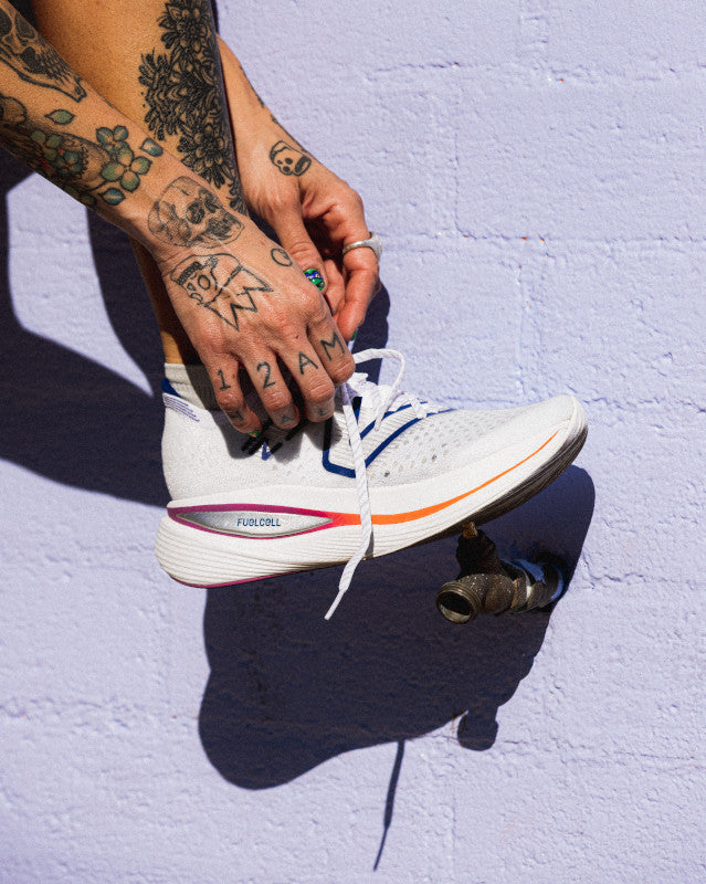 A model tying her shoe laces on the New Balance Women's Fuel Cell SuperComp Trainer in the color White/Victory Blue/Magenta Pop