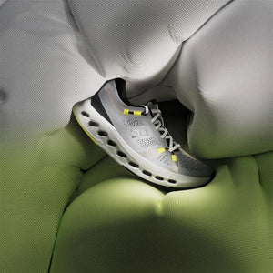 Grey ON running shoe in the middle of a plush looking comforter in grey and green hues