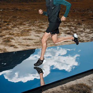 Photograph of a male runner's legs on a surface mirroring the sky and clouds on a desert landscape