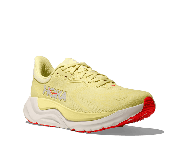 Yellow running shoe with red sole on a green background