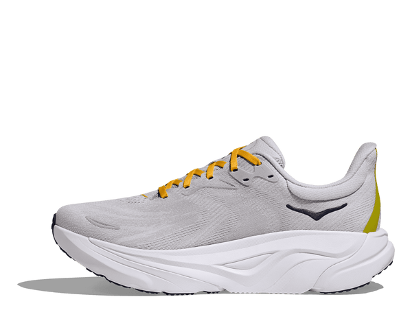 The Hoka logo is stitched near the ankle on the medial side of the upper using black thread. 