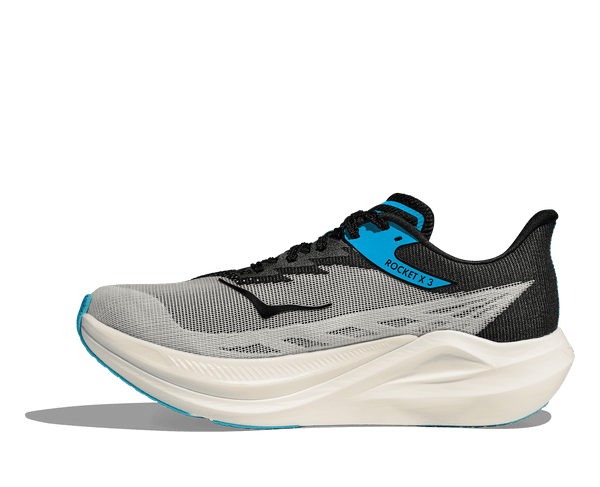 A Hoka logo is stitched near the toe on the medial side of the upper in black thread. 