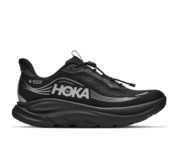A black Hoka running shoe with a thick black sole, featuring a prominent silver HOKA logo and a small Gore-Tex Whisper label on the side, shown against a plain white background.
