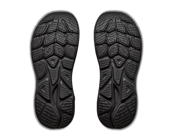 A pair of black shoe soles shown from the bottom against a solid green background.