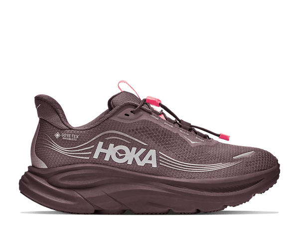 A Hoka running shoe in a muted plum-brown colorway, featuring a textured mesh upper, a thick cushioned sole, and bright pink laces