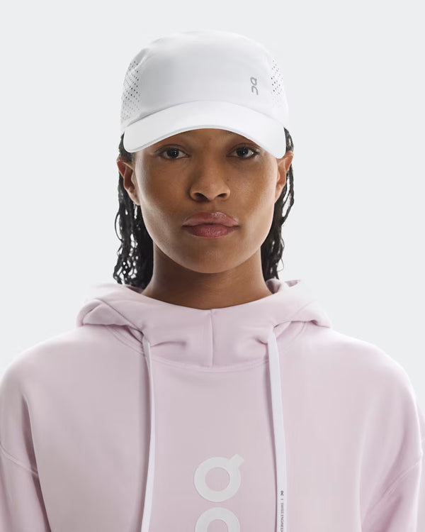 Person wearing a light pink hoodie and white cap on a plain background
