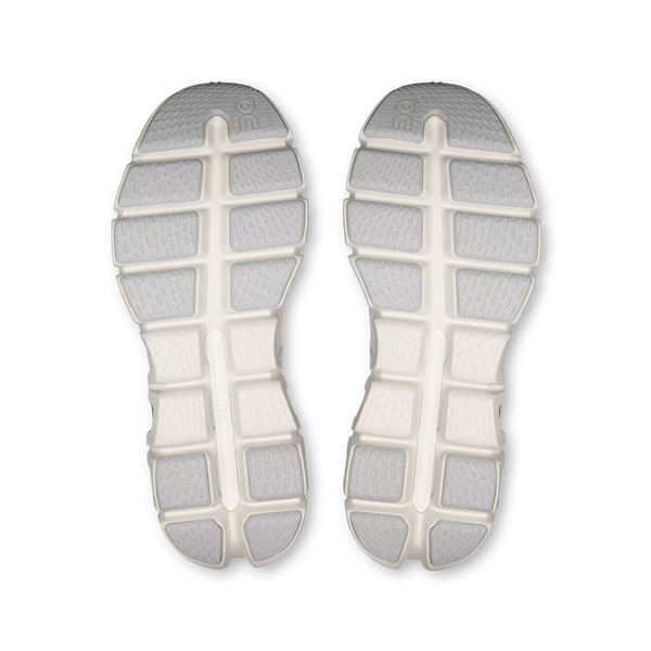 The soles of a pair of shoes, shown from a top-down view. The soles are off-white with light gray textured grip sections arranged in a grid pattern.