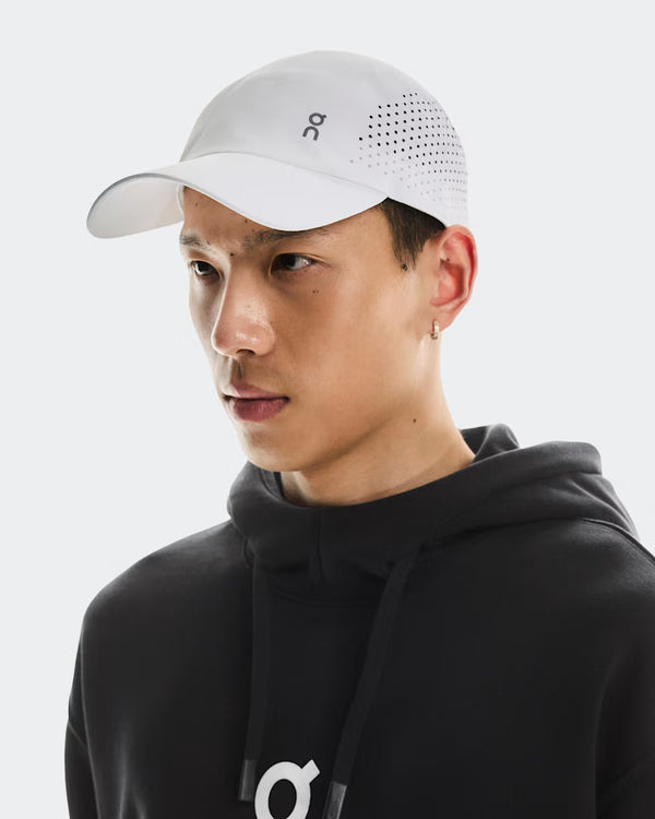 Person wearing a black hoodie and white cap with a logo on a light gray background
