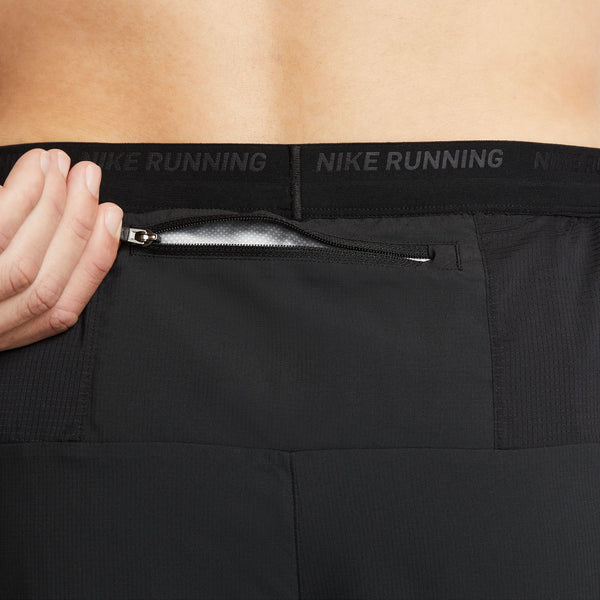 Black Nike Running pants with a hand opening a zipper pocket on a beige background