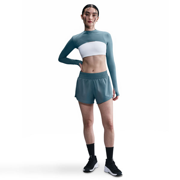 Woman wearing a teal long-sleeve top and shorts with a white sports bra on a white background