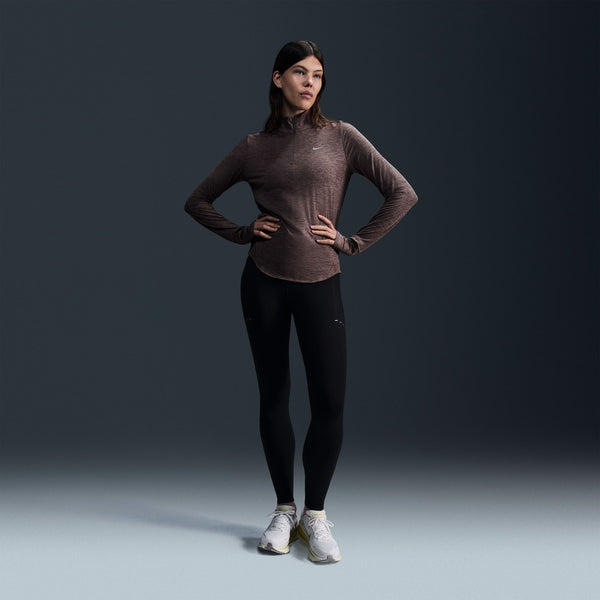 Woman wearing a brown long-sleeve top and black leggings on a gray background