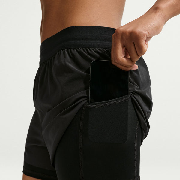 Person wearing black athletic shorts with a pocket on a light gray background