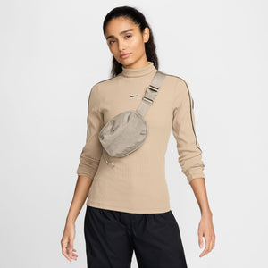 Woman wearing a beige long-sleeve shirt with a Nike logo and a matching waist bag on a white background
