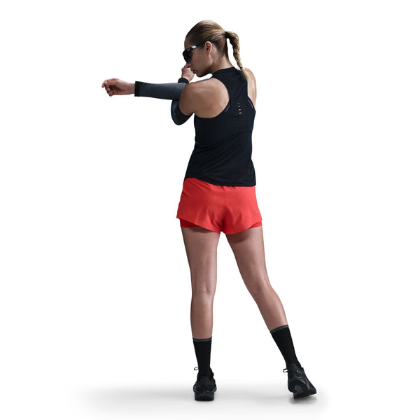 Woman in black tank top and red shorts stretching on a white background