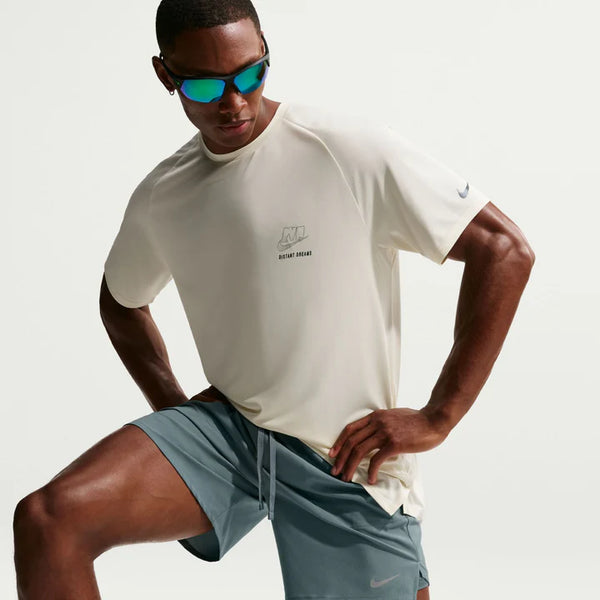 Man wearing a beige t-shirt and gray shorts with sunglasses on a light gray background
