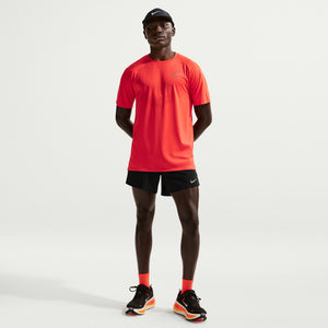 Man wearing a bright orange running shirt and black shorts on a light gray background