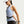 A woman in athletic wear wearing a light blue sleeveless Nike tank top and a black waist bag, shown from the side against a light gray studio background.