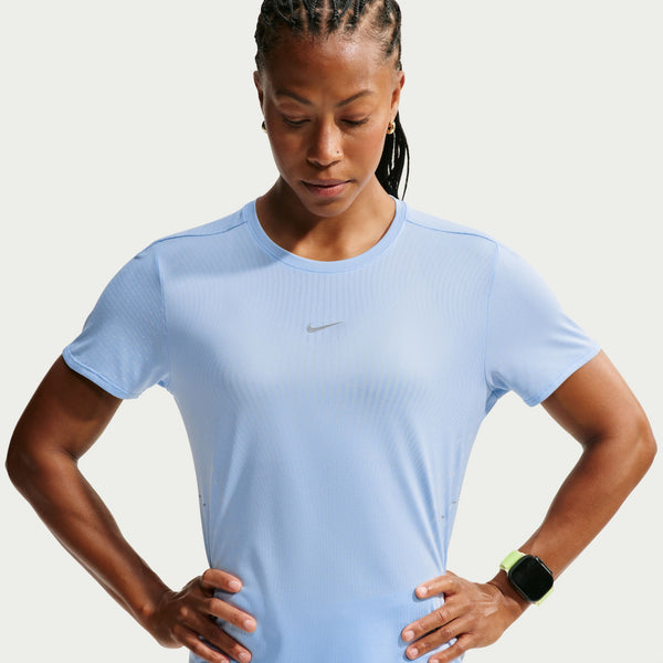 A woman wearing a light blue Nike athletic short-sleeve shirt, standing with hands on hips against a light gray studio background.