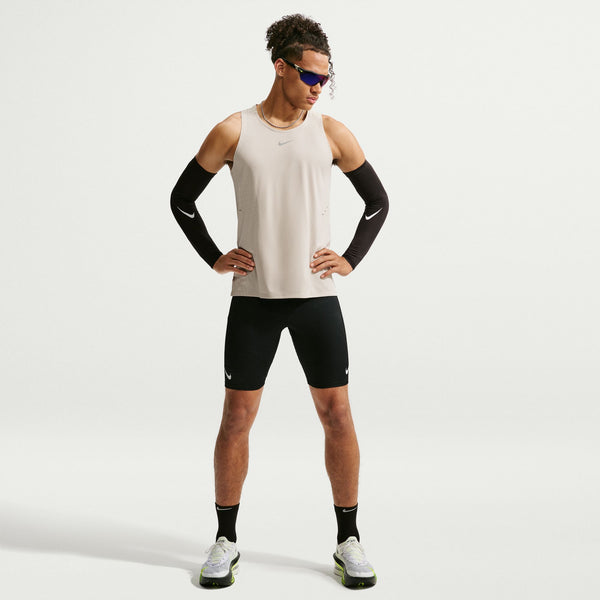 Man wearing a beige tank top, black shorts, and black arm sleeves on a white background