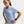 A woman wearing a light blue Nike athletic short-sleeve t-shirt, white running sunglasses with pink lenses, and a smartwatch, posed against a light gray studio background.