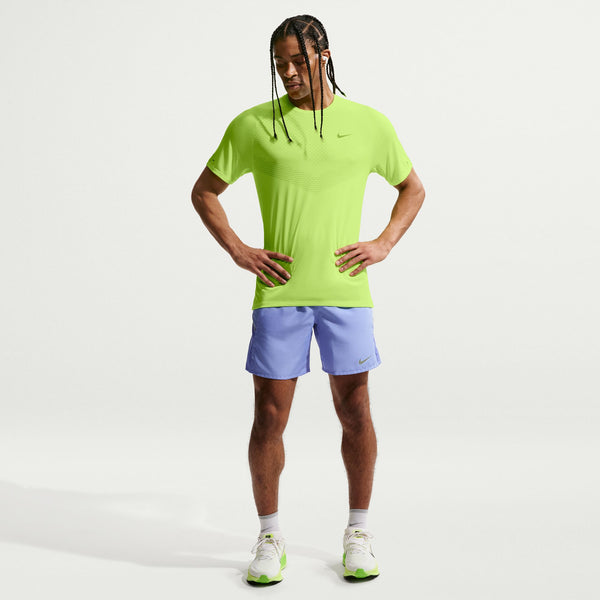 A man modeling a bright neon yellow-green Nike short-sleeve athletic shirt and light blue athletic shorts against a clean white studio background.
