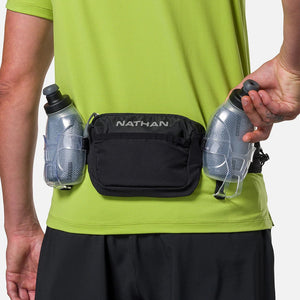 Person wearing a black Nathan waist pack with two water bottles on a plain background