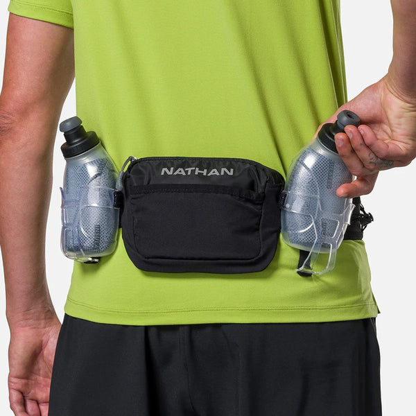 Person wearing a black Nathan waist pack with two water bottles on a plain background