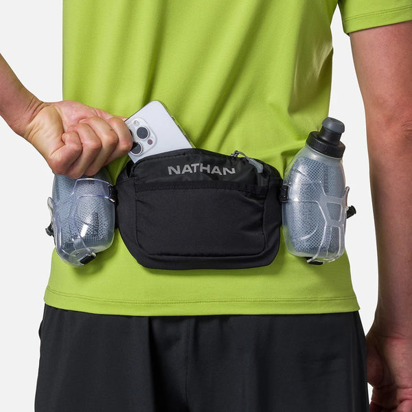Person wearing a black waist bag with Nathan branding, holding a phone and water bottle.