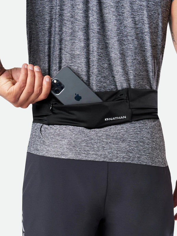 Person wearing a black waist pack with a phone in it, on a plain background