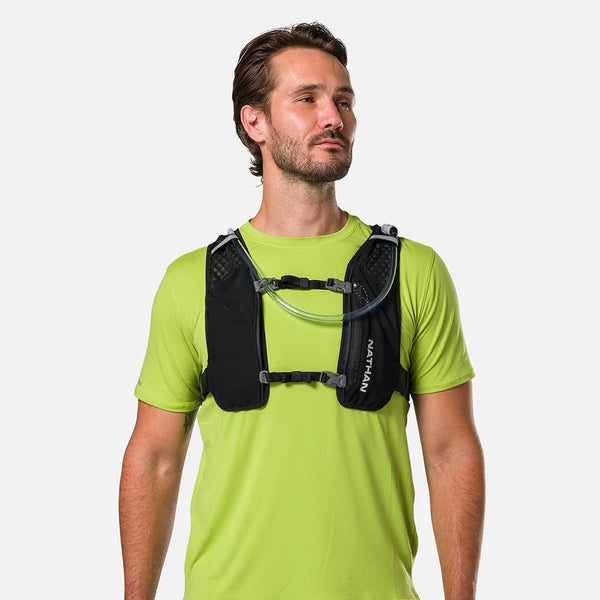 Man wearing a green shirt with a black hydration vest on a white background