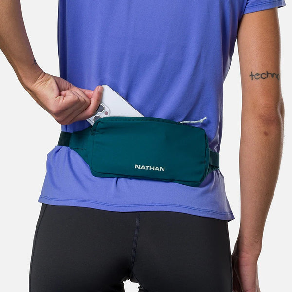 Person wearing a blue shirt and black shorts with a green waist bag featuring the 'Nathan' brand.