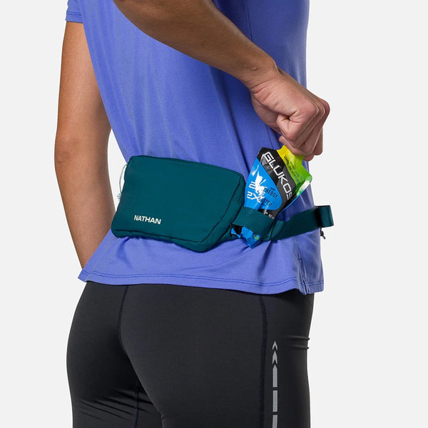 Person wearing a green waist bag with Nathan branding, holding energy gels.