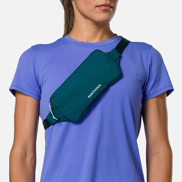 Person wearing a green waist bag with 'Nathan' branding on a plain background