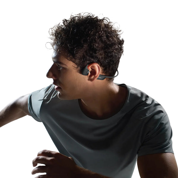 Person wearing a gray t-shirt and wireless earbuds on a white background