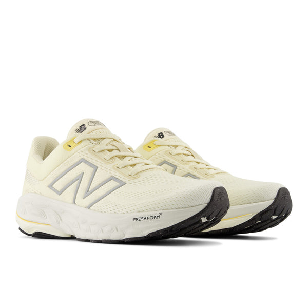 A pair of light yellow running shoes set at an angle with a black outsole.