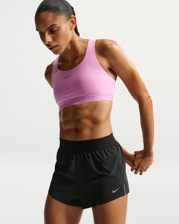 Woman wearing a pink sports bra and black shorts with Nike logo on a white background