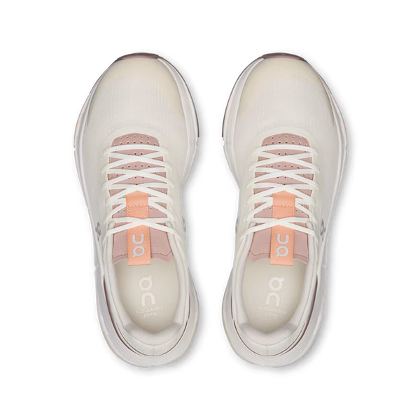 A pair of On Cloudrunning sneakers shown from a top-down view. The shoes feature a light beige and white mesh upper with a soft pink collar lining and a peach-colored tongue label displaying the 'on' logo.