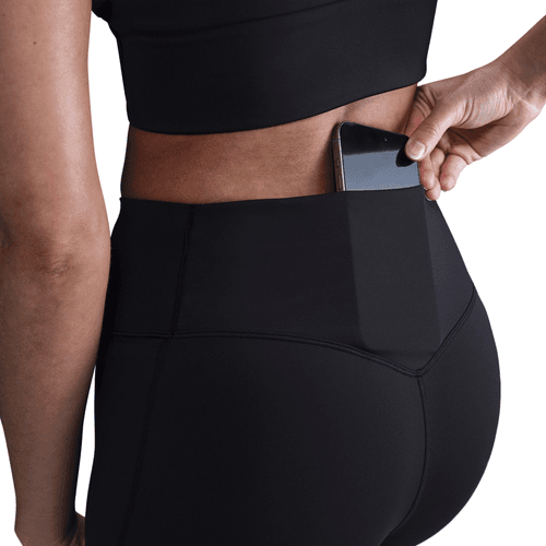 Person wearing black athletic leggings with a pocket holding a phone on a white background